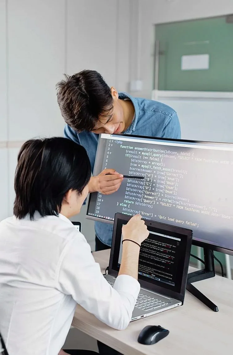 二人の人物がモニターに映るプログラムコードを指しながら話し合っている様子